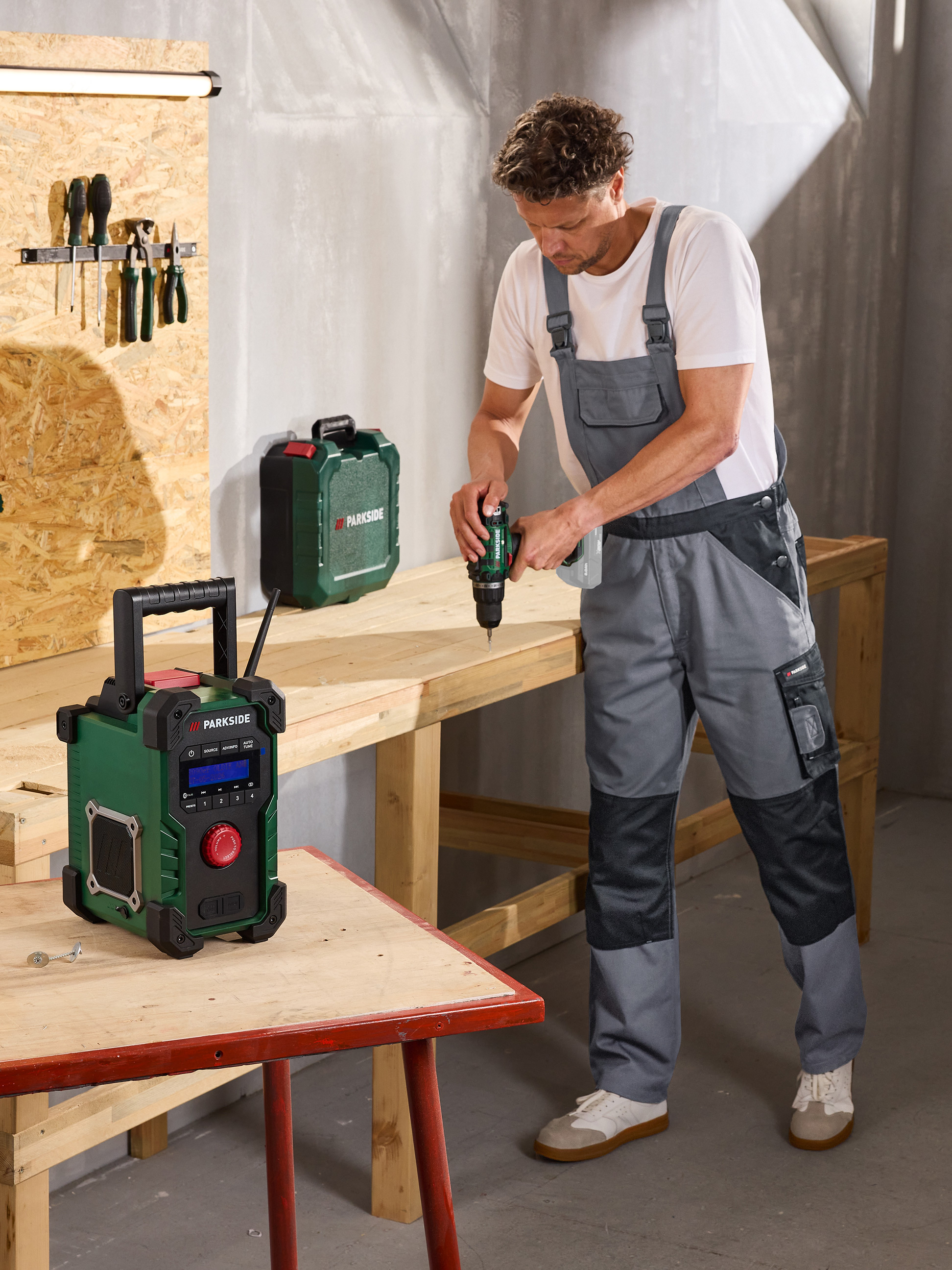 Mann bohrt in Holz, mit Radio und Werkzeugkoffer in einer Werkstatt.