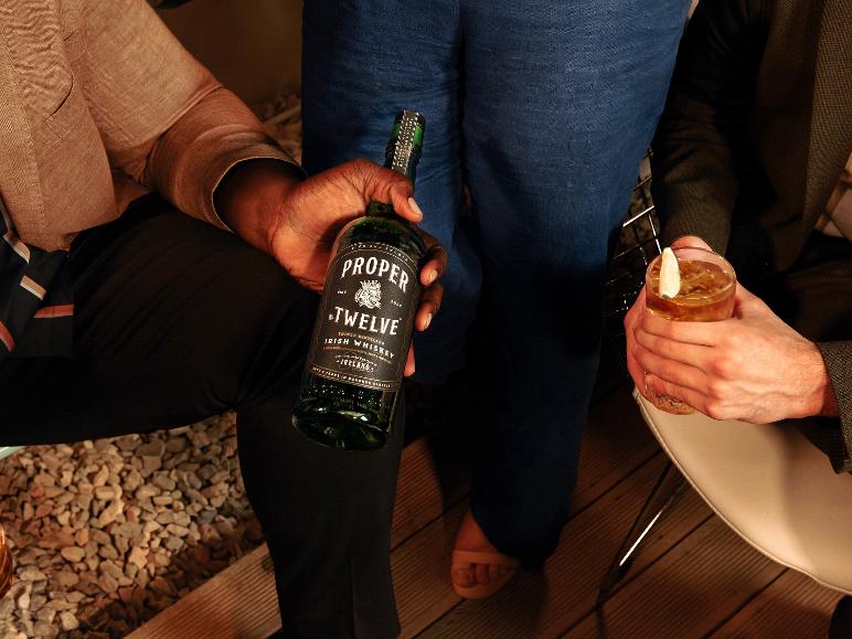 Ein Mann hält eine Flasche irischen Whiskey, und ein anderer Mann hält ein Glas Cocktail.