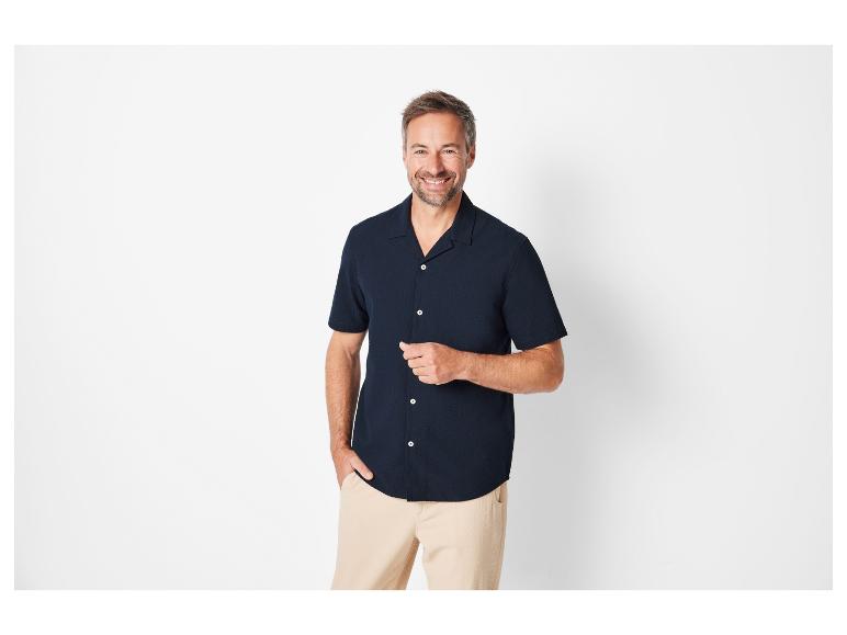 Ein Mann trägt ein kurzärmeliges Hemd und eine beige Hose.