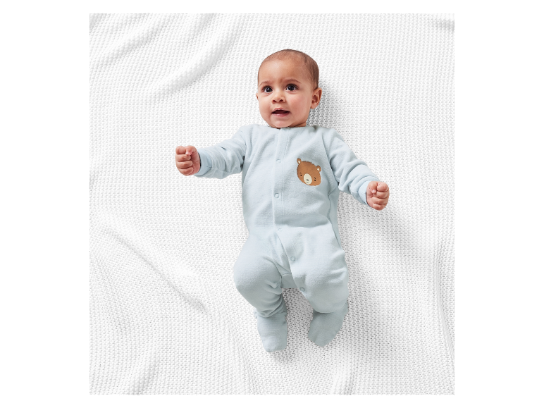 Süßes Baby liegt auf einer weißen Strickdecke in einem hellblauen Strampler mit Bär.