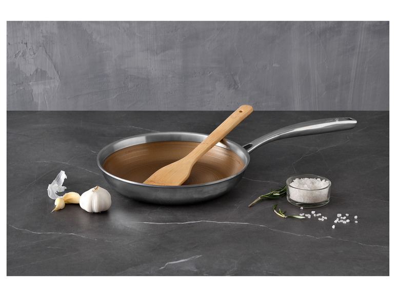 Eine Bratpfanne mit einem Holzlöffel, Knoblauch und Salz auf einer grauen Arbeitsplatte.