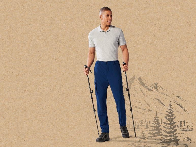 Ein Mann mit Wanderstöcken und blauen Hosen in einer Berglandschaft.
