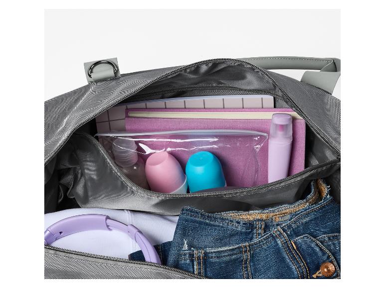 Helle graue Reisetasche mit Toilettenartikeln, Kopfhörern und Jeans.