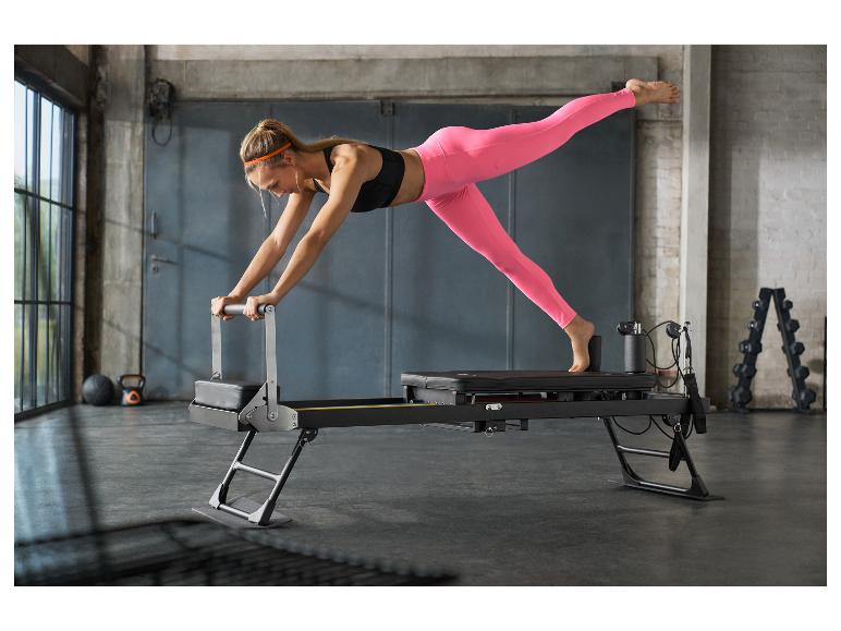 Frau macht Pilates auf einem schwarzen Reformer in einem Fitnessstudio.