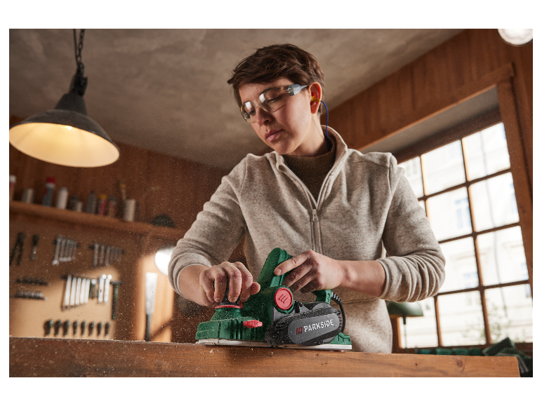 Eine Frau verwendet einen Parkside Hobel, um Holz in ihrer Werkstatt zu bearbeiten.