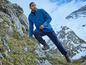 Ein Mann in einer blauen Fleecejacke und dunkelblauen Hosen, wandert über einen felsigen Berg