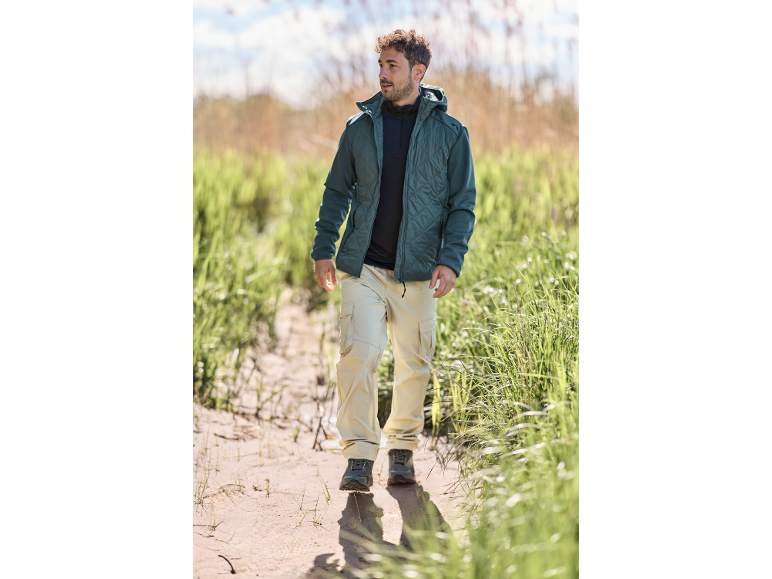 Mann in Steppjacke und beiger Cargohose geht auf einem Sandweg.