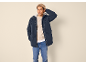 Mann in dunkelblauem Parka, beigem Pullover, Jeans und Mütze