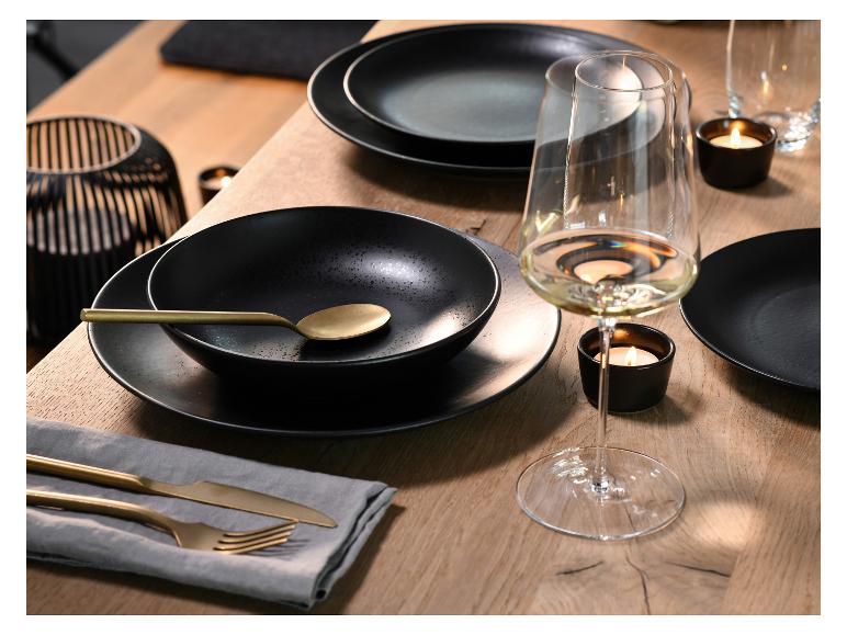 Holztisch mit schwarzem Geschirr, goldenem Besteck, Weingläsern und Kerzen.