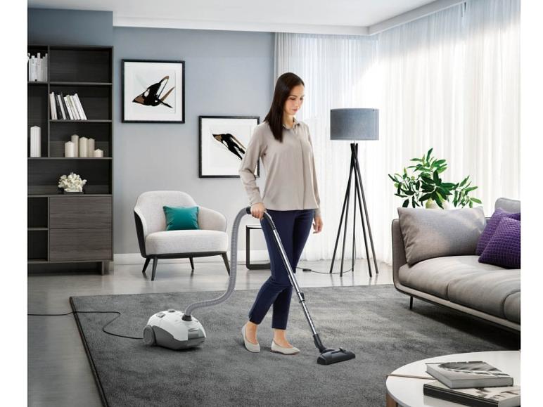 Frau saugt einen grauen Teppich in einem modernen Wohnzimmer.
