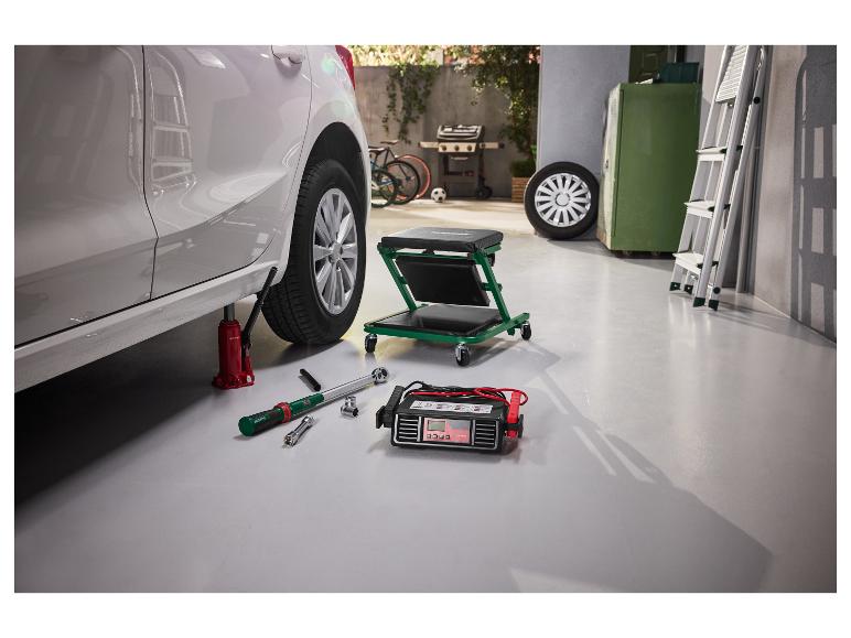 Wagenheber, Drehmomentschlüssel und Batterieladegerät in einer Garage beim Reifenwechsel.