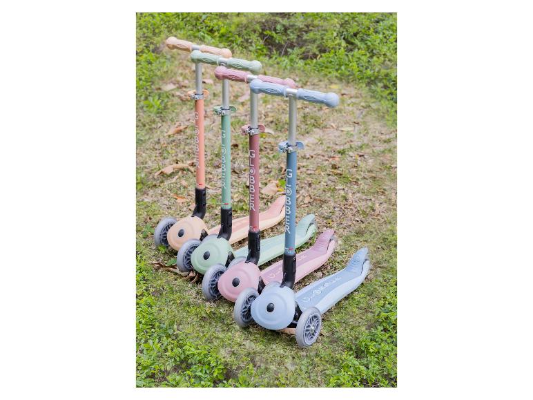 Fünf bunte Roller mit je drei Rädern, aufgereiht auf Gras.