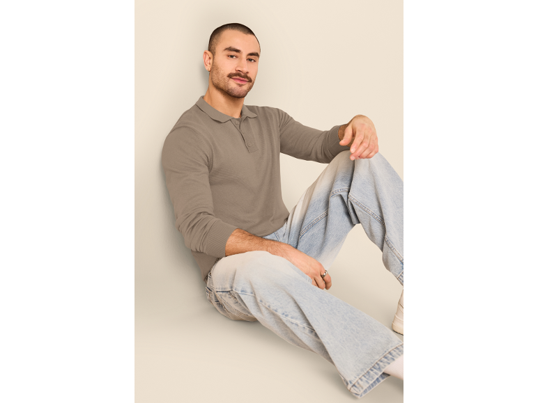 Mann in einem Langarm-Poloshirt und hellen Jeans, auf dem Boden sitzend.