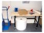 Eine Packstation mit Karton, Luftpolsterfolie, Klebebandabroller und Sackkarre.