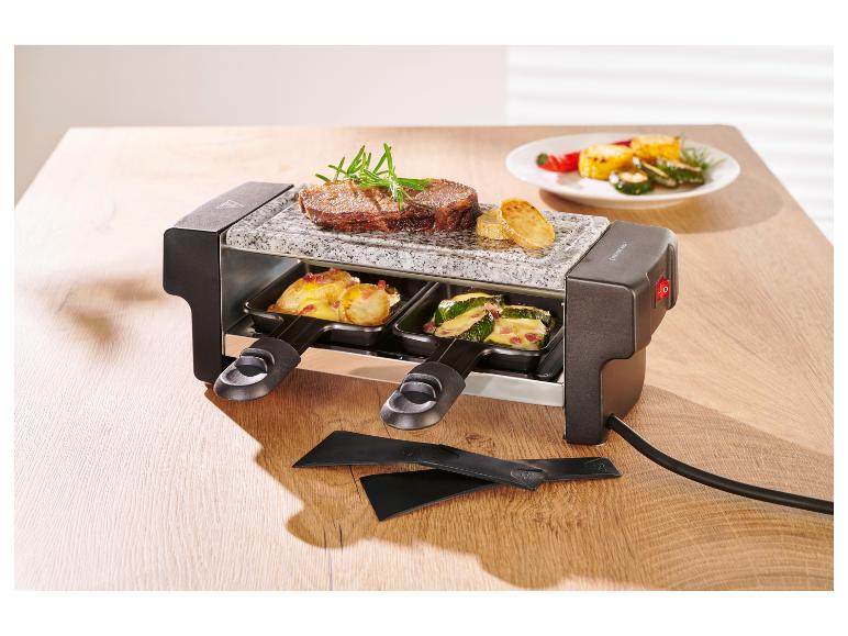 Raclette-Grill mit Steak, Kartoffeln und Zucchini auf einem Holztisch.