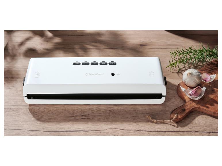 Weißes Vakuumiergerät auf einem Holztisch mit Knoblauch und Rosmarin.