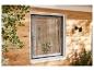 Fenster mit Insektenschutzgitter an Holzwand, mit Pflanzen und Sonnenlicht.