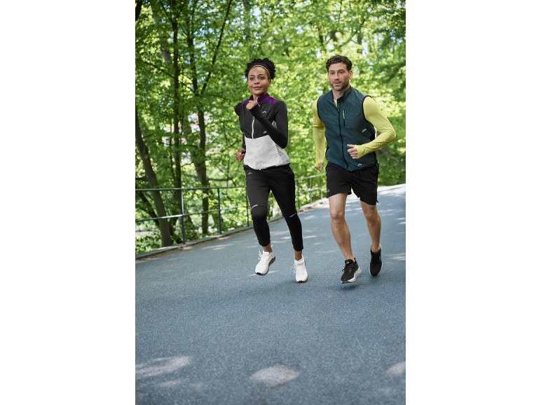 Zwei Läufer in Sportkleidung joggen draußen, Frau in Jacke und Mann in Weste.