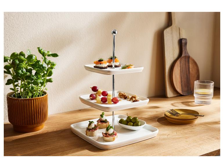 Ein dreistöckiger Servierständer mit verschiedenen Vorspeisen, daneben ein Basilikumtopf und Küchenutensilien.