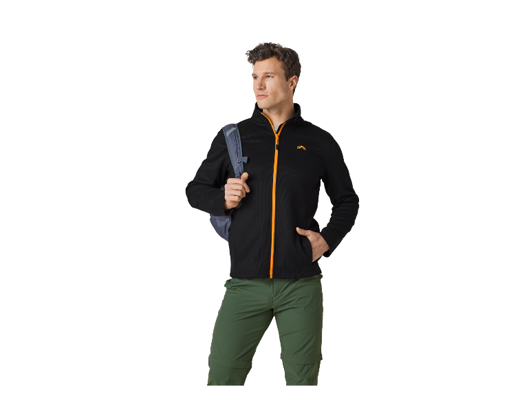 Mann in schwarzer Fleecejacke und grüner Hose, mit Rucksack über der Schulter.