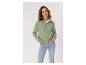 Frau in einer grünen Strickjacke mit Reißverschluss und Jeans, Hände in den Taschen.