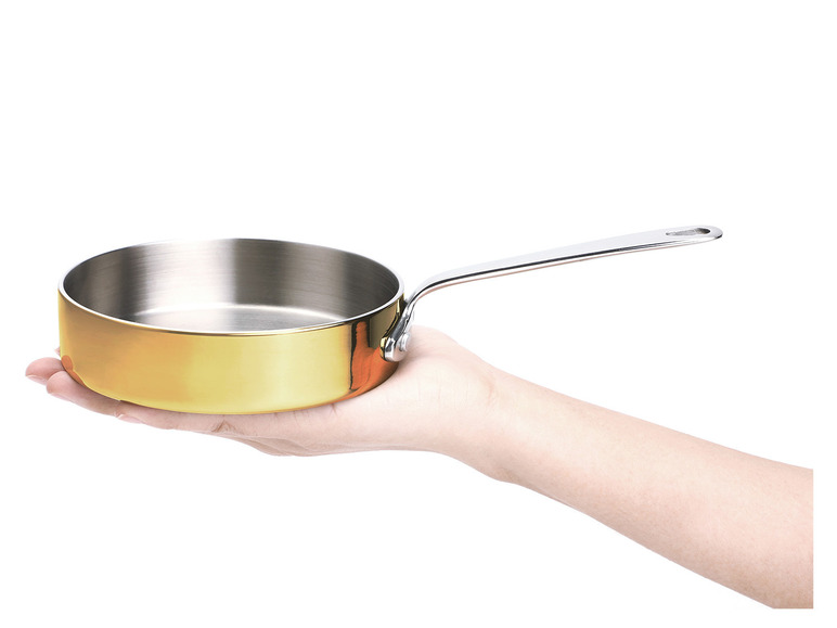 Eine goldene Pfanne mit Griff in einer Hand.