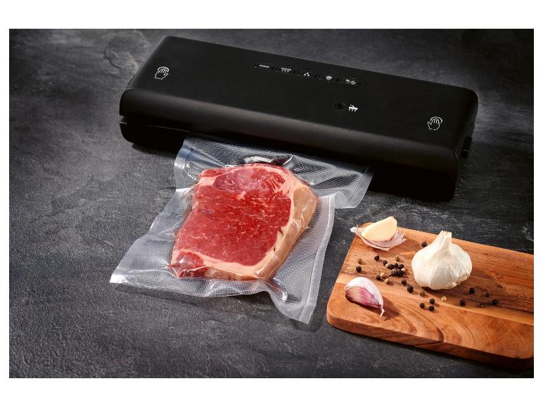 Schwarzes Vakuumiergerät mit einem versiegelten Stück Rindfleisch und Knoblauch auf einem Schneidebrett.