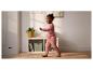 Kind in rosa Outfit läuft in einem Zimmer mit Regal und Pflanze.