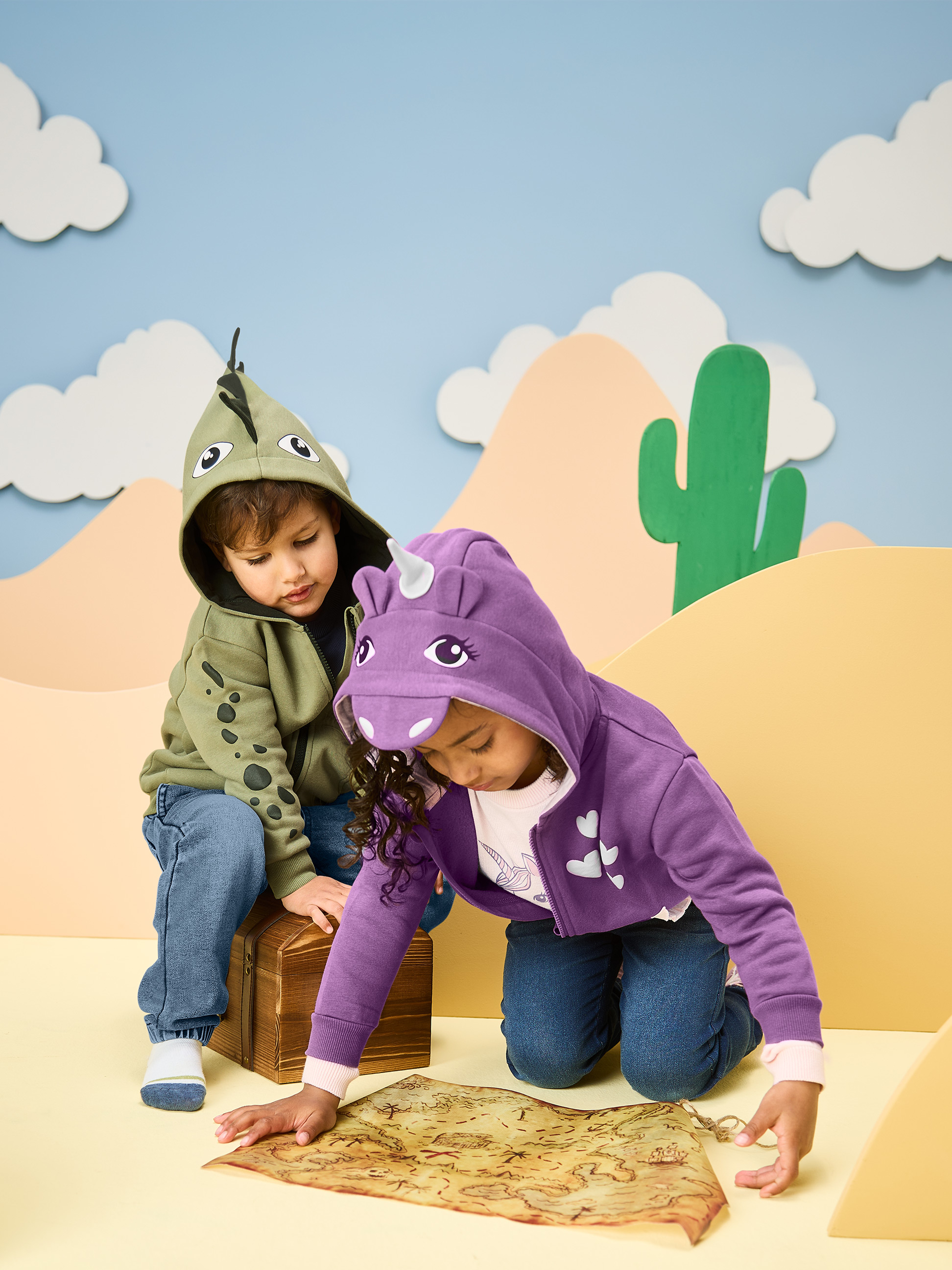 Kinder in Dinosaurier- und Einhorn-Hoodies, die eine Schatzkarte betrachten.
