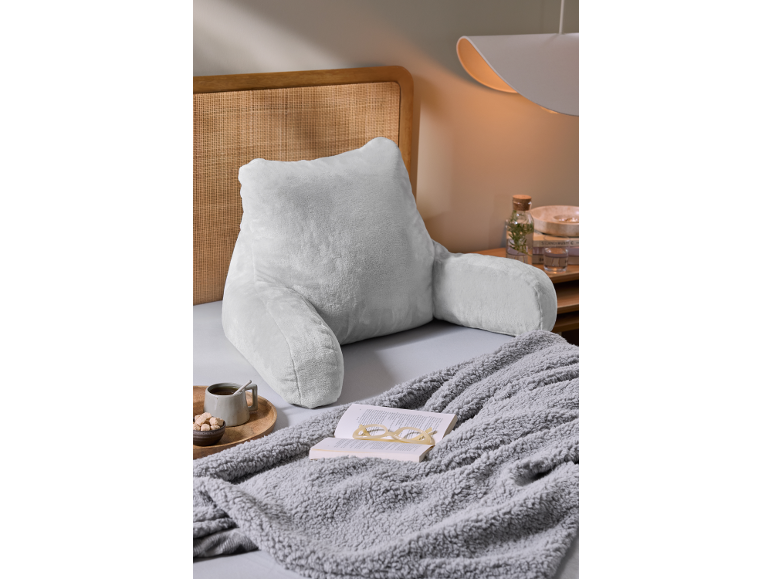 Hellgraues Lesekissen mit Armlehnen auf einem Bett mit Decke und Buch.