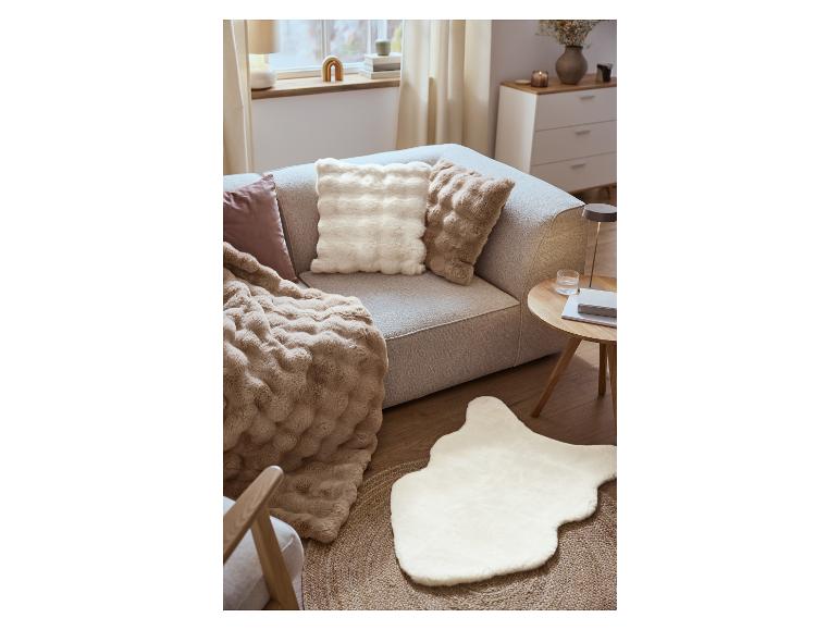 Ein graues Sofa mit flauschigen Kissen und einer weichen Decke, neben einem Couchtisch und einem Fellteppich.