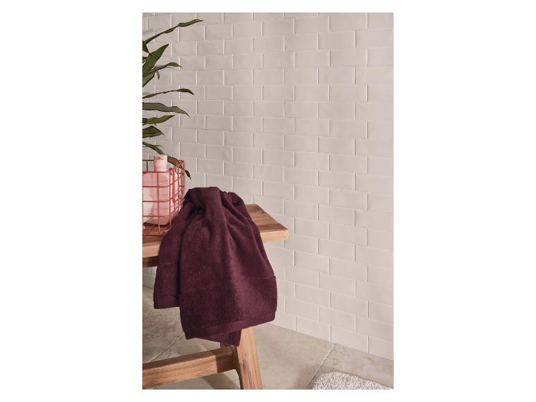 Badetücher auf einer Holzbank, mit gefliesten Wänden und einer Pflanze.