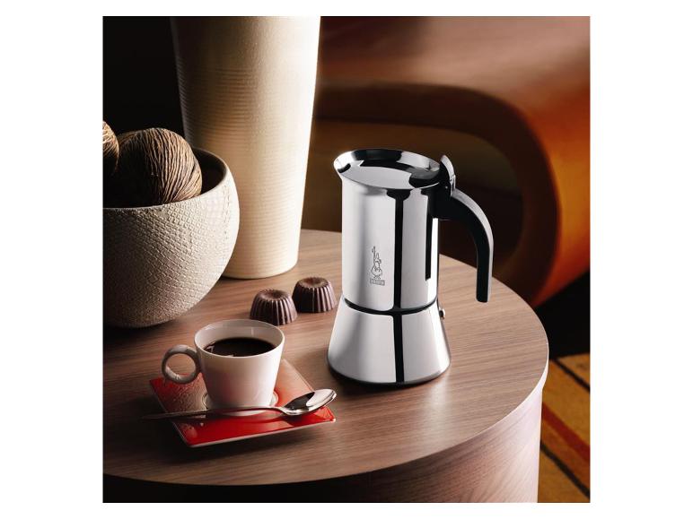 Silberne Mokkakanne, Tasse Kaffee und Schokoladenpralinen auf einem Holztisch.