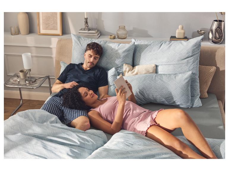 Frau im rosa ESMARA Pyjama liest ein Buch im Bett neben ihrem Partner.