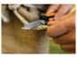 Hände schneiden Seil mit einem Messer, mit Jute-Stoff im Hintergrund.