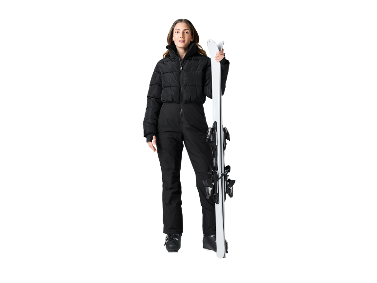 Eine Frau im schwarzen Skianzug hält weiße Skier