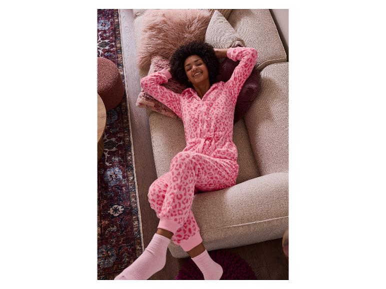 Frau in rosa Leoparden-Overall, auf einem beigen Sofa liegend.