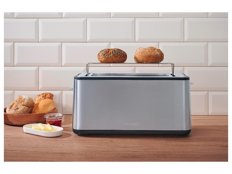 Edelstahl-Toaster mit zwei Brötchen oben, Butter und Marmelade auf einer Holztheke.