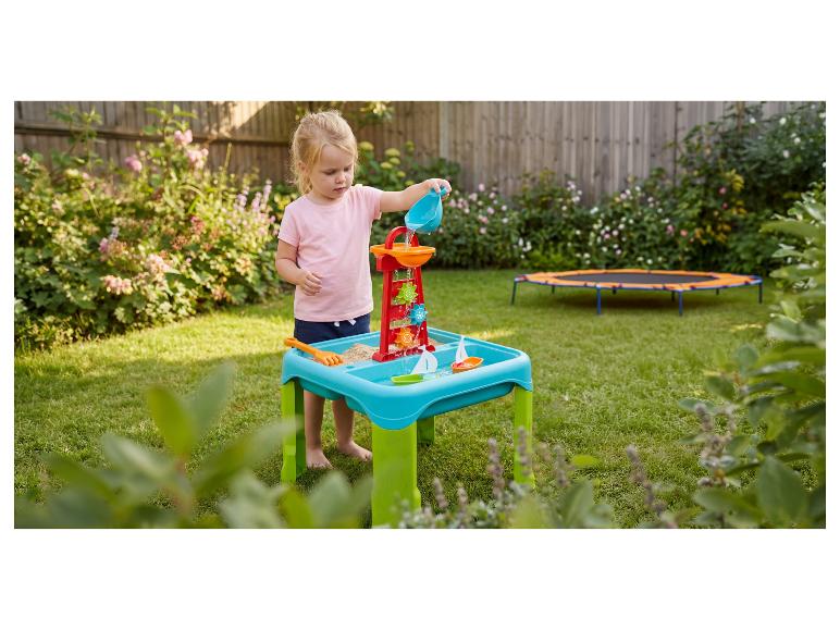 Mädchen spielt mit Wasser-Sand-Tisch mit Mühle und Booten im Garten.