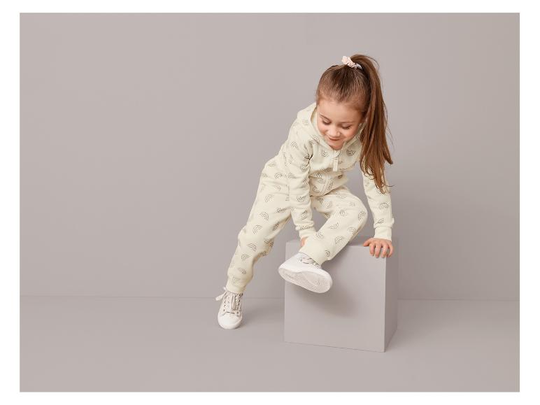 Ein Mädchen trägt einen weißen Hoodie und Jogginghose mit Regenbogenmuster.