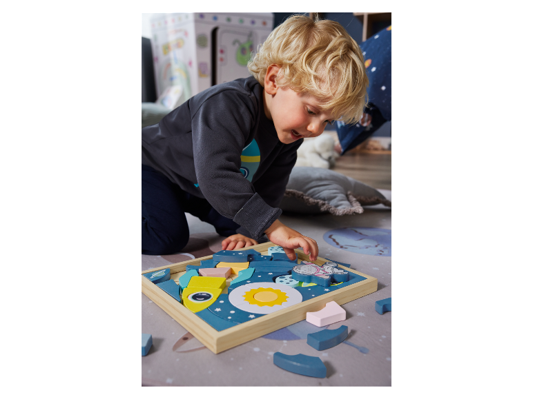 Junge spielt mit einem Holzpuzzle zum Thema Weltraum auf einem Teppich.