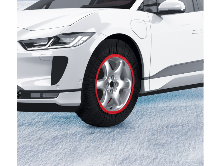 Weißes Elektroauto mit roten Textil-Schneeketten auf Schnee.
