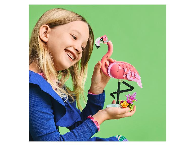 Ein lächelndes Mädchen hält einen rosa Baustein-Flamingo und Blumen.