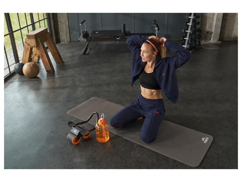 Frau in Sportkleidung auf Yogamatte mit Wasserflasche und Trainingsgerät.