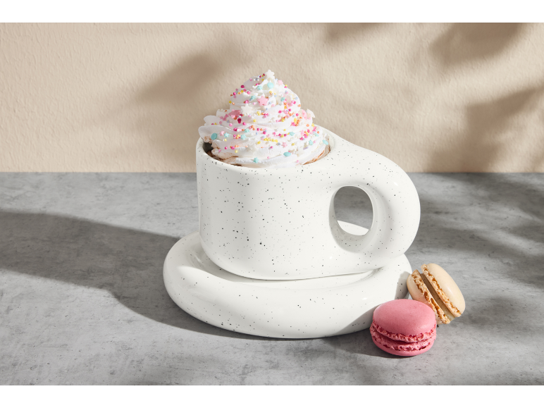 Weiße Tasse mit heißer Schokolade, Schlagsahne und Streuseln, mit rosa und beigen Macarons.