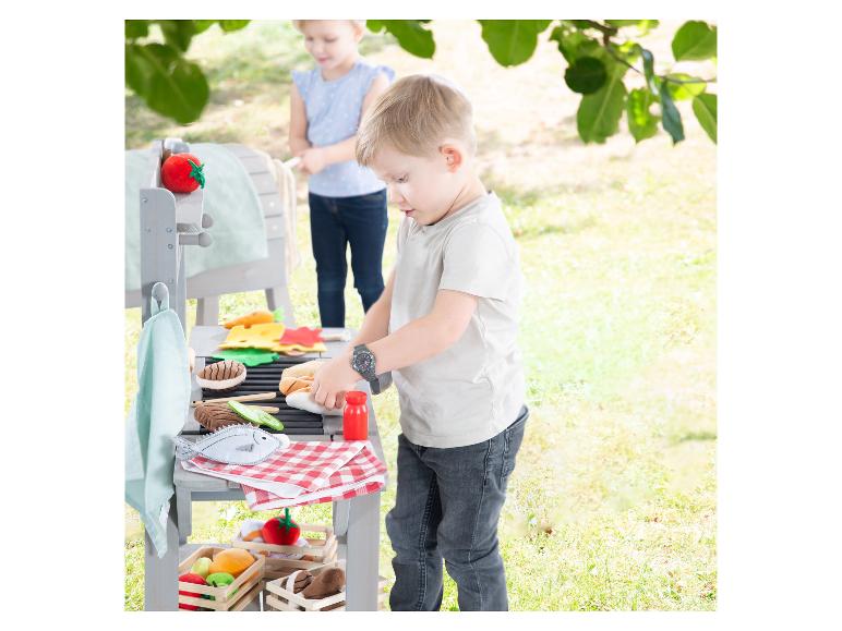 Kinder spielen draußen mit einem Spielzeuggrill und Filzessen.