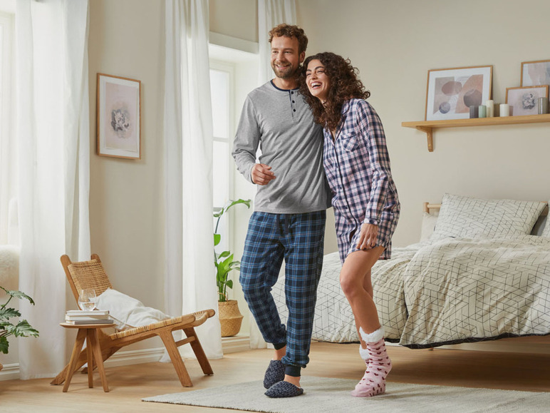 Ein Paar in Pyjamas, der Mann in einem grauen Oberteil und blauen Hosen, die Frau in einem karierten Pyjama.