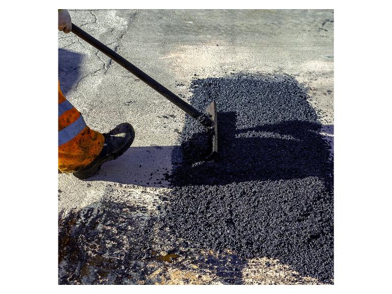 Arbeiter verteilt Asphalt mit einer Schaufel auf der Straße