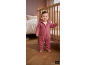 Baby in einem rosa Kapuzenoverall steht an einem Holzbettchen im Kinderzimmer.