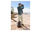 Mann in Jacke und Cargohose blickt mit Fernglas am Strand, mit Rucksack und Wasserflasche.